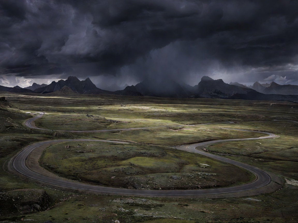 Beartooth Highway crossing a high treeless plateau with dark storm clouds building over distant peaks