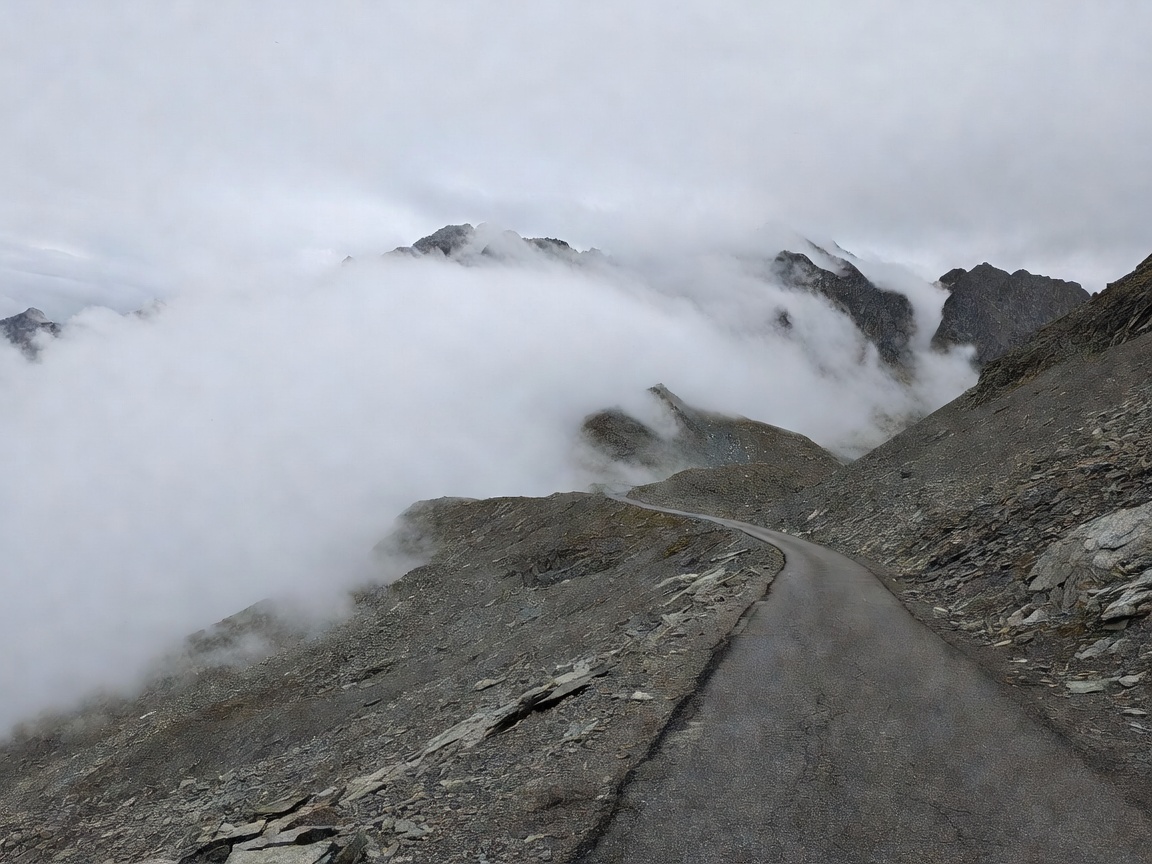 Bare high-altitude road near the Col de l'Iseran summit with cloud rolling over scree slopes